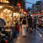 Bangkok street food stalls serving customers at dusk in a busy city neighbourhood