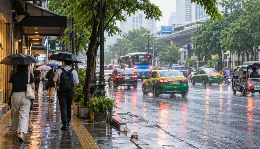 People walking with umbrellas beside Bangkok traffic during a normal tropical rain shower