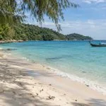 Quiet white-sand beach on Ko Samet with clear water and a Thai long-tail boat offshore