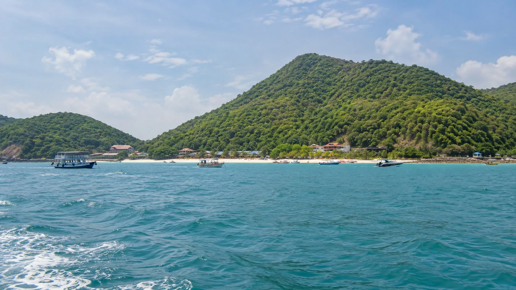 View of Koh Larn from the sea with forested hills, beach and boats