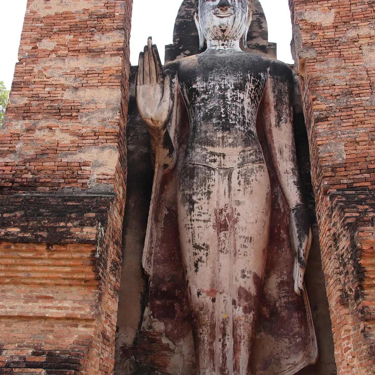 Standing Buddha framed by brick ruins in Sukhothai Historical Park