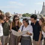 A closed group of travellers reviewing a Thailand itinerary with a local coordinator beside the Chao Phraya River
