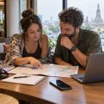 Travellers planning a Thailand route with a map and laptop